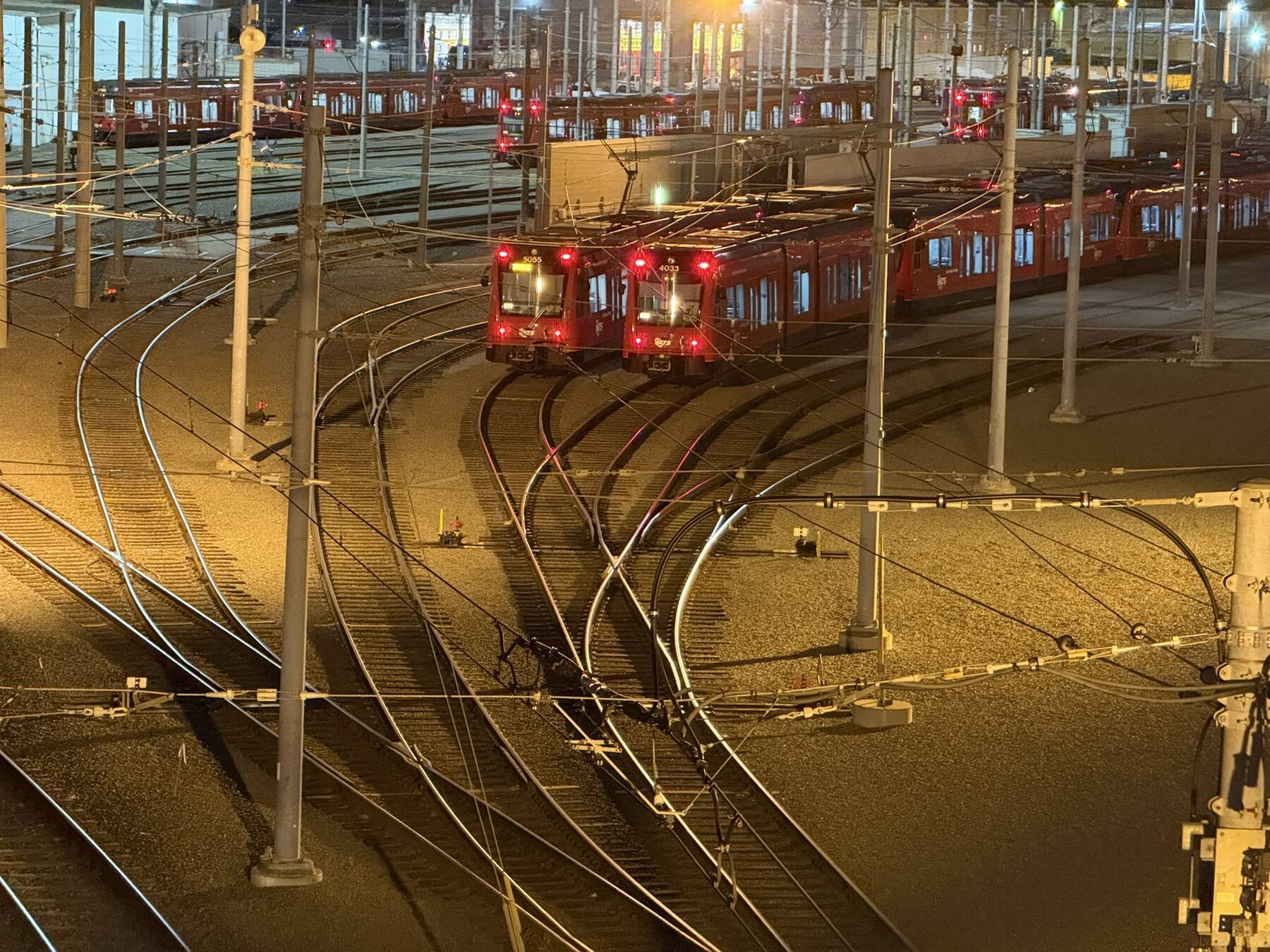 San Diego MTS light rail trains at night in the rail yard, with curving tracks and overhead wires